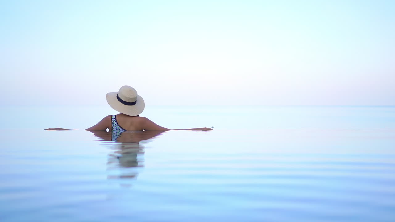 Rückansicht einer unkenntlichen Frau in einem Infinity-Pool mit Weichzeichnung.