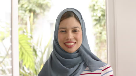 Retrato-De-Una-Mujer-Birracial-Sonriente-Con-Hijab-En-Casa-Con-Espacio-Para-Copiar,-Cámara-Lenta