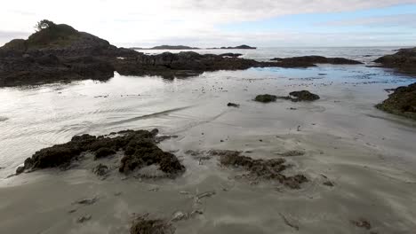 Luftaufnahme-Von-Einer-Drohne,-Die-Tief-über-Nassem-Sand,-Felsen-Und-Gezeitenbecken-In-Richtung-Offenes-Wasser-An-Der-Küste-Von-Vancouver-Island-In-Der-Nähe-Des-Dorfes-Tofino-Fliegt