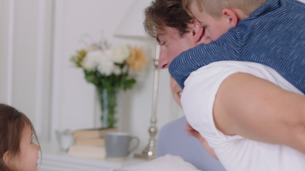 행복한 가족과 아이들이 침대에 뛰어들고 엄마와 아빠와 함께 놀고 아들을  ⁇ 에  ⁇ 고 주말 아침에 재미를 느끼고 흥분된 어린 아이들이 집에서 부모와 함께 게임을 즐기고 있습니다.