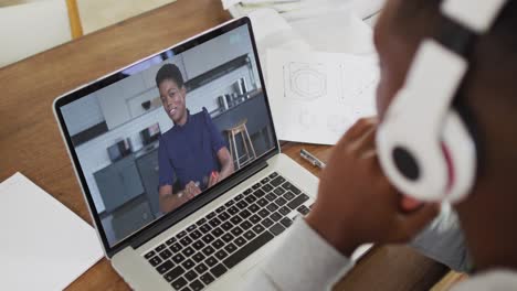 estudiante universitario afroamericano que sostiene notas mientras hace una videollamada en una computadora portátil en casa