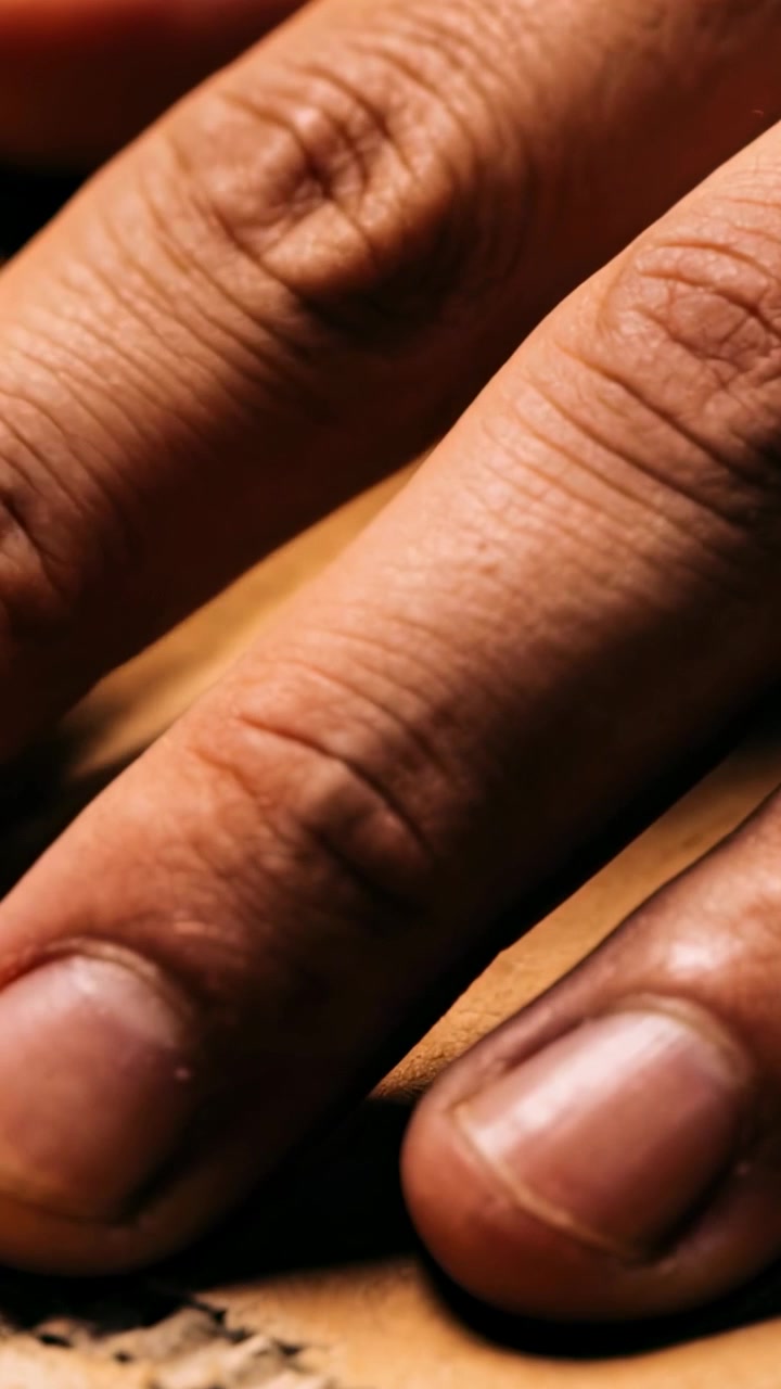 Vertical video: Landing right-hand fingers sliding along stitched leather seam, inspecting grain