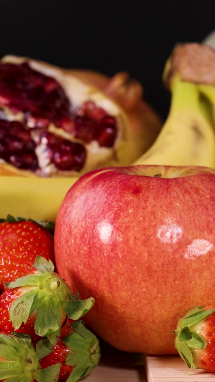 En levende vertikal presentasjon med skivet mango, kiwi, jordbær og granateplefrø.