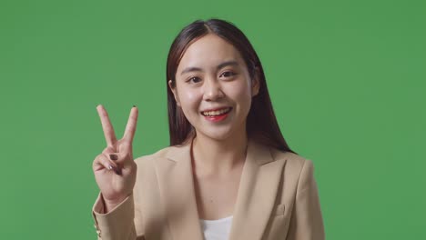 close up of asian business woman showing gesture peace and smiling while standing on green screen in the studio