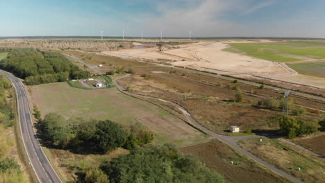 camino rural a través del campo con turbinas eólicas y zona minera en el fondo, vista aérea
