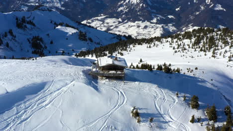 Vista-Aérea-Panorámica-Alrededor-De-Un-Chalet-En-La-Cima-De-La-Montaña-En-La-Nieve-En-Un-Día-Soleado