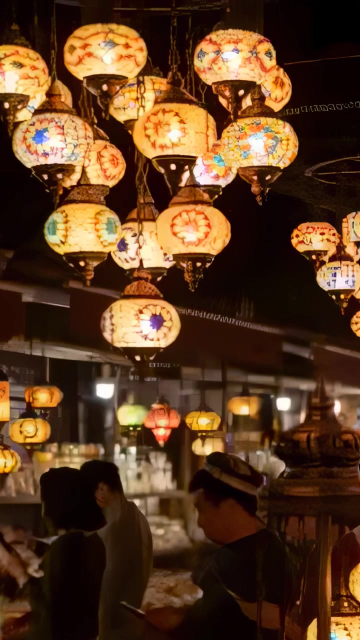 Vertical video: Pulling cam from tight shot, showing mosaic lamps above busy market person on phone