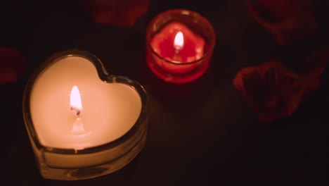 disparo de arriba de románticas velas rojas encendidas en forma de corazón en el fondo cubiertas de pétalos de rosa 1