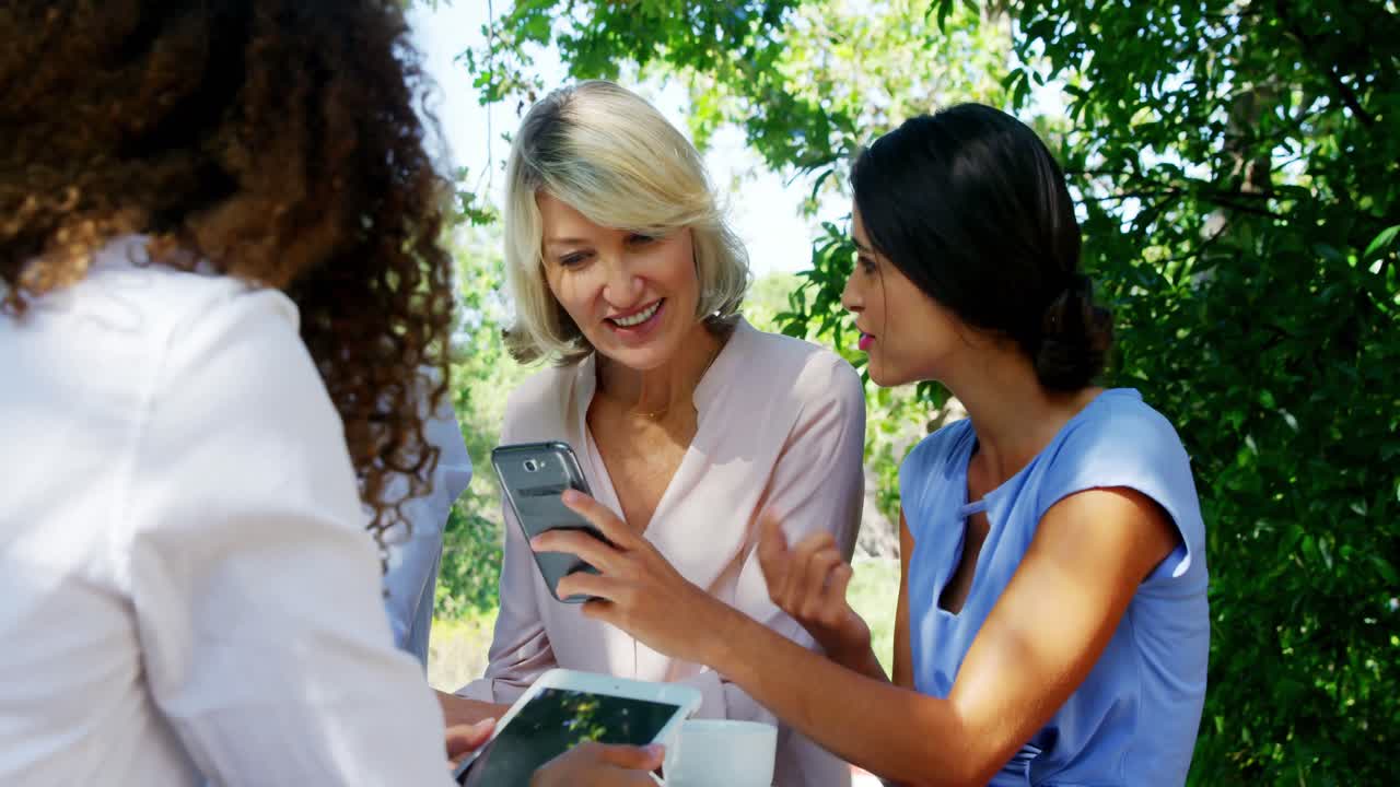 Female friends discussing over mobile phone at outdoor caf&Atilde;&copy;