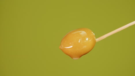 close-up of a candied olive on a wooden stick with dripping liquid