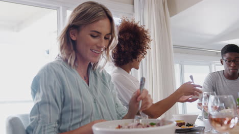 Group-Of-Young-Friends-Sitting-Around-Table-At-Home-Enjoying-Meal-Together