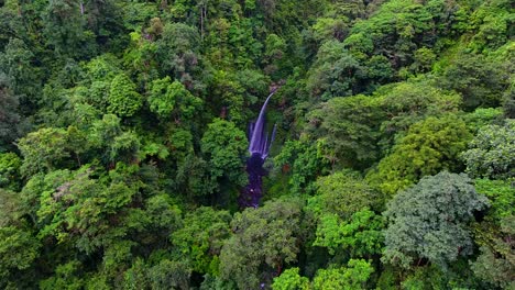 aerial view of tiu kelep waterfall, in middle of indonesian jungle, cloudy day, in lombok, asia - approaching, drone shot