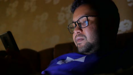 Young-man-sitting-on-sofa-using-smart-phone-at-night