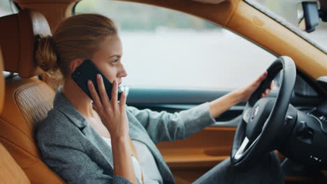 business woman talking phone behind steering wheel. female executive using phone