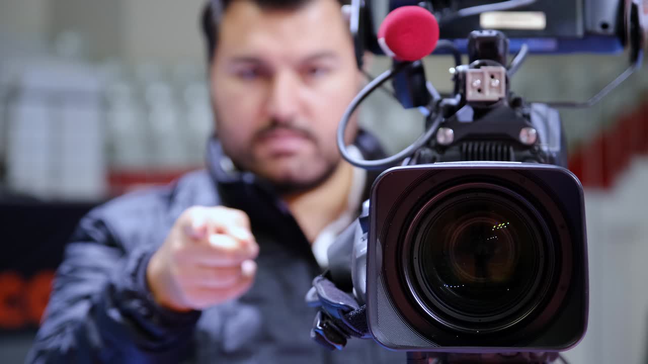 The cameraman counts down and points to a live television broadcast with his finger