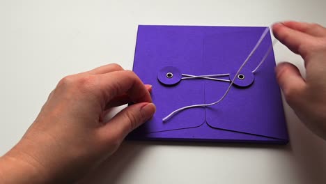 person unties thin lace on blue paper envelope or folder