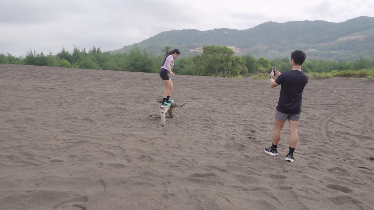 Couple taking photos of a woman balancing on driftwood in sand dunes
