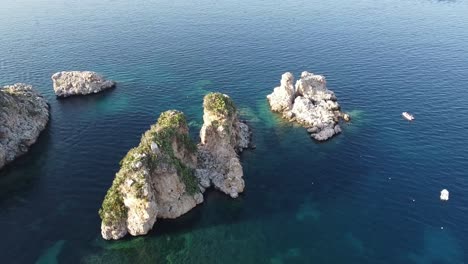 faraglioni, stacks of scopello by the calm water of castellammare del golfo in trapani, sicily, italy