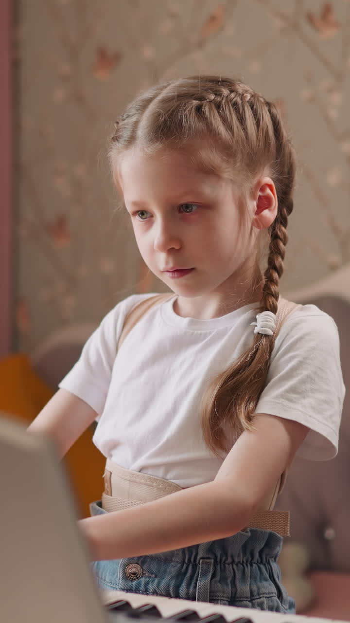 Girl in orthopedic corset finishes playing composition on electronic piano and lowers hands. Serious child looks at sheet music standing in cozy room