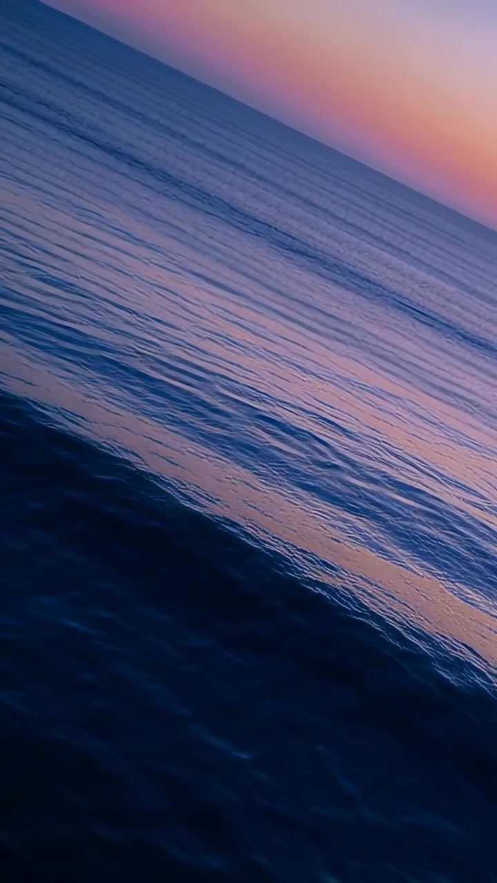 Vertical video: Tilting camera at sea showing ocean surface and horizon reflecting pink-purple sky