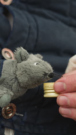 male hand gives lid with elixir to cute toy mouse. small animal sits in owner vest. village squire has fun giving pet enchanting liquid closeup