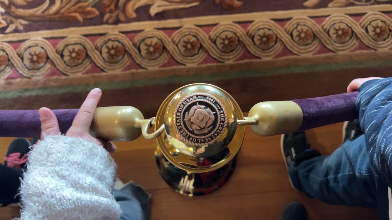 투어 그룹 과 아이 들 이 보라색 벨 ⁇  로프 로 놀고 있는 것 처럼 청동 또는 금 게시물 위 에 있는 상징 이나 봉인 을 내려다보고 있다