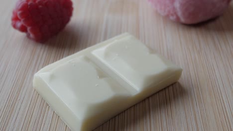 white chocolate bar on a wooden table with fresh raspberries nearby