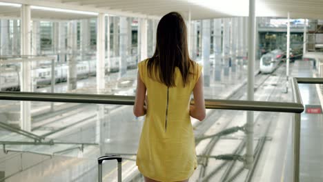 happy beautiful girl with travel bag or suitcase on wheels in hand standing at railway station in madrid. 4k