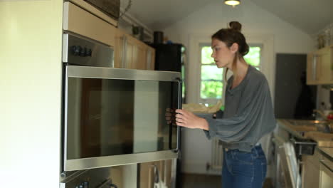 young woman places baking tin in oven