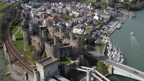 An-aerial-view-of-Conwy-Castle-on-a-sunny-day,-flying-right-to-left-around-the-castle-while-zooming-in-with-the-town-in-the-background,-North-Wales,-UK
