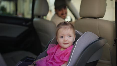 a baby girl in a car seat, looking at the camera