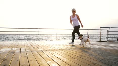 young woman running with cute dog jack russel near the sea