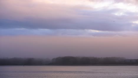 niebla sobre el mar y la ciudad costera al amanecer con aguas tranquilas y cielo colorido