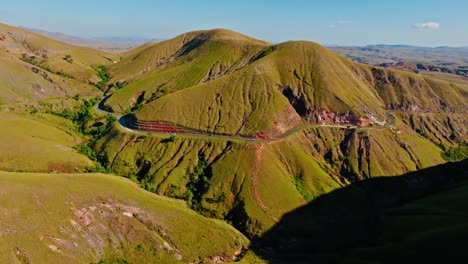 aerial view of rolling green hills and a winding road cutting through a remote mountainous valley in madagascar, offering stunning natural scenery and tranquil atmosphere.