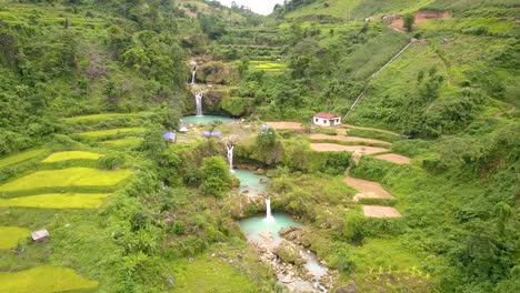 Waterfall-in-the-mountains-in-Vietnam,-cascading-water-ponds-formed-with-water-flowing-down-the-mountain-side,-surrounded-by-agricultural-fields