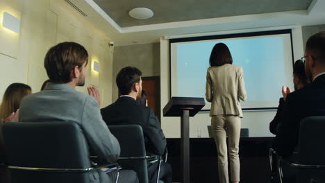 rear view of caucasian businesswoman entering in a conference room while people clapping, then she comes up on the podium