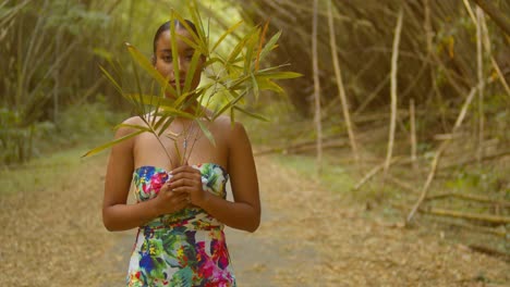 young woman in a flower dress walks forward while holding a bamboo leaf in her hand