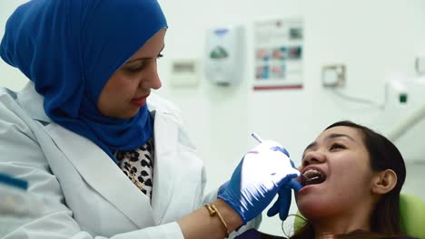 female muslim dentist working and checking the teeth of an asian patient at the dental clinic in dubai, uae. - close up shot