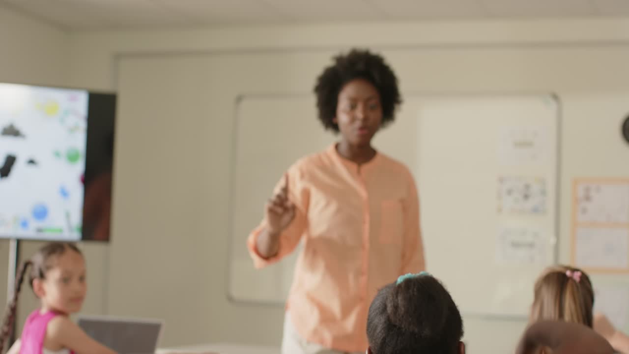African American woman teacher calling on students raising hands to answer, pointing at whiteboard