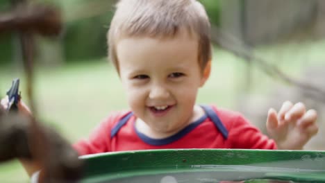 Little-caucasian-boy-dancing-and-smiling-outdoors-next-to-a-barrel-of-water,-SLOMO,-RACK-FOCUS