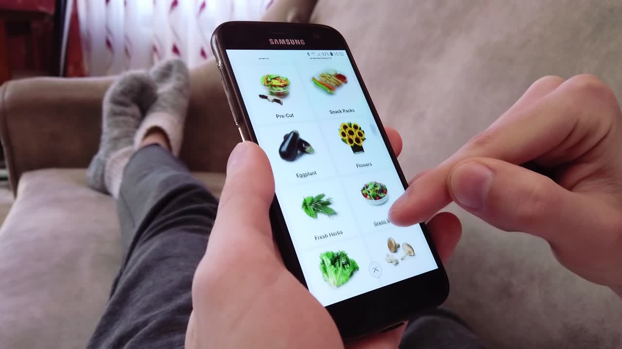 CHISINAU, MOLDAVIA - 8 APRILE 2020: uomo che sceglie verdure da un negozio di alimentari online mentre è seduto sul divano di casa. Idea sul coronavirus