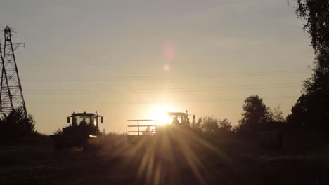 silhouette of distant farmers on driving tractors on horizon in rural countryside at sunset