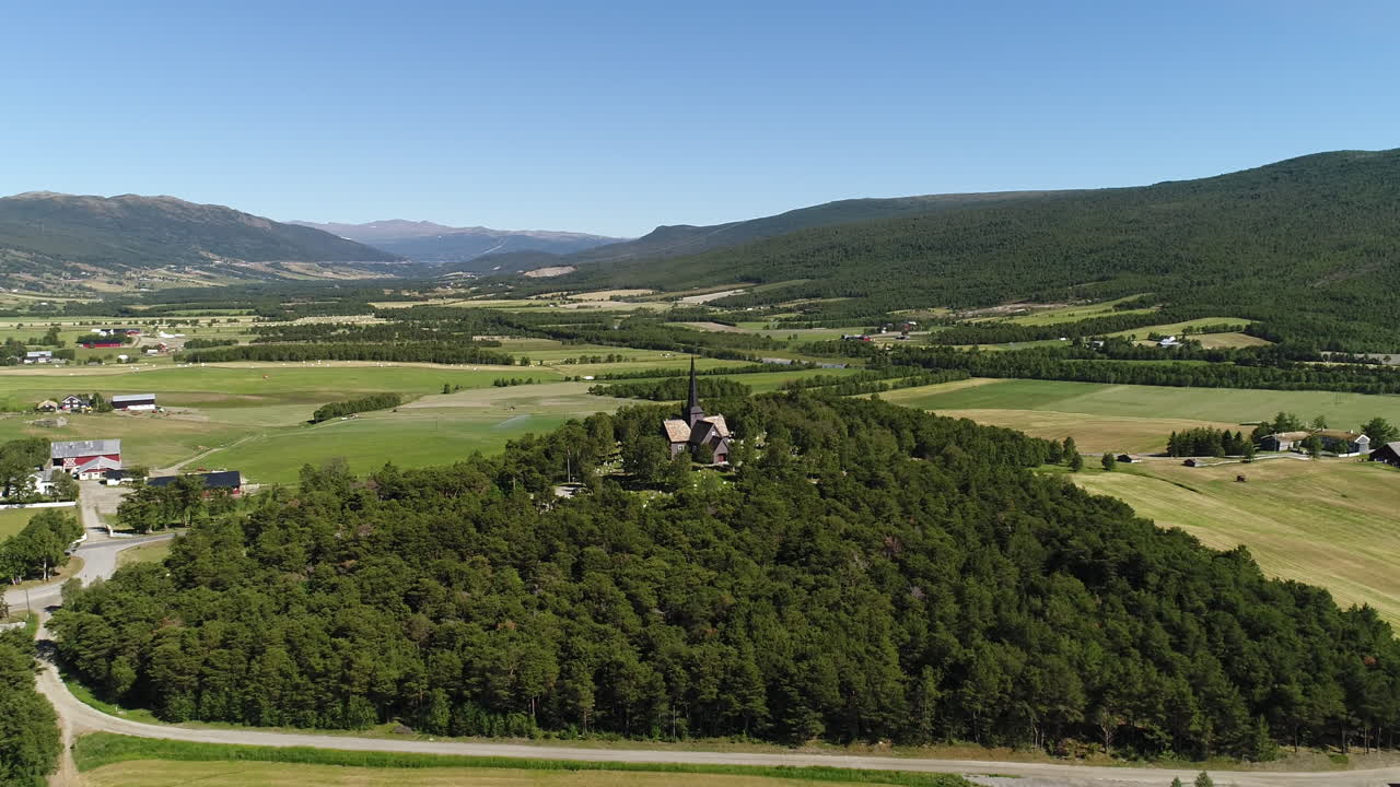 fotografía de un avión no tripulado de una vieja iglesia de madera en medio de vegetación y tierras de cultivo abiertas. filmado en noruega durante el verano.