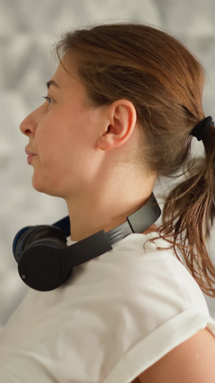 헤드폰을 착용 한 여성이 집에서 조을 하고 있습니다. 무선 헤드폰이있는 여성은 국내 체육관에서 트레드밀에서 훈련합니다. 스포츠 여성은 운동을 즐기고 있습니다.