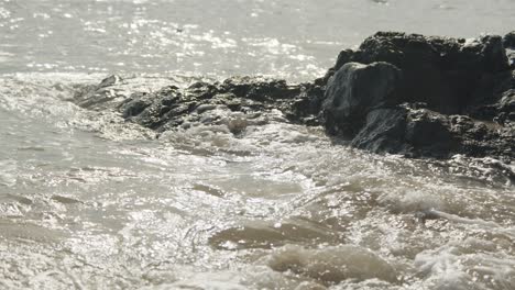 Waves-crashing-against-old-volcanic-black-rock-during-a-warm-summer-day,-abstract-background