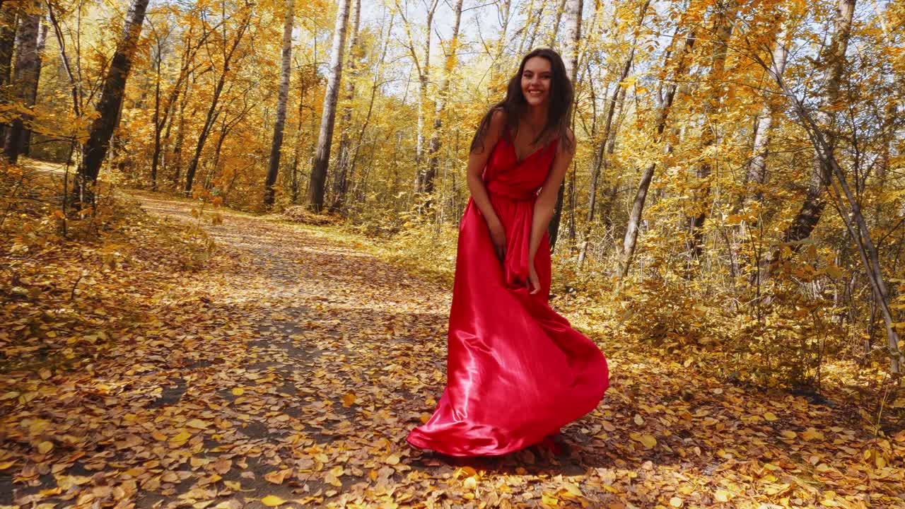 Un viaggio radioso: cattura l'eleganza di una donna in un abito rosso fluente tra il fogliame autunnale dorato di una foresta serena