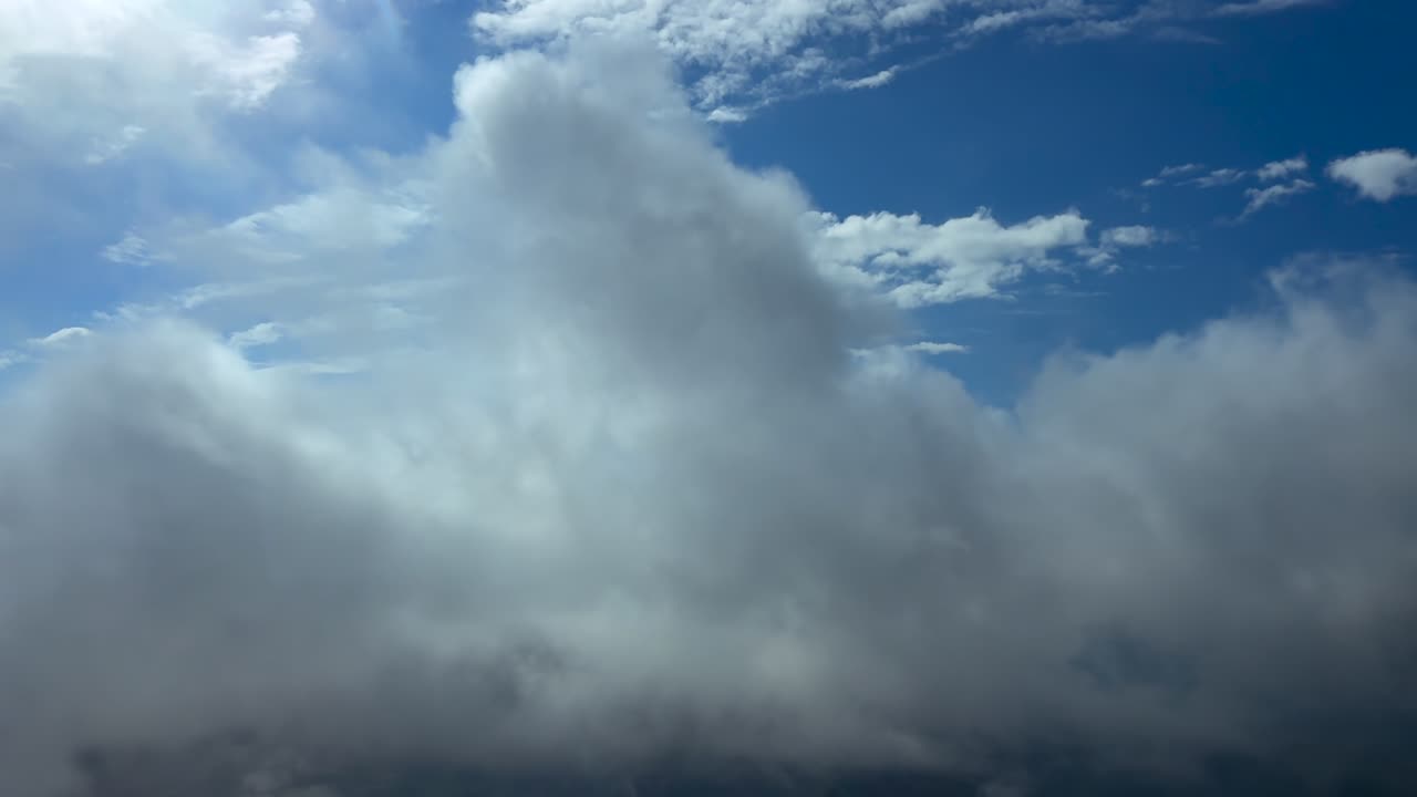 An immersive pilot’s perspective from the cockpit of a jet airplane flying peacefully through ethereal broken stratus clouds under a deep blue sky