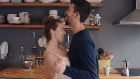 Happy-young-couple-newly-wed-dancing-listening-to-music-in-kitchen-wearing-pajamas-morning-at-home