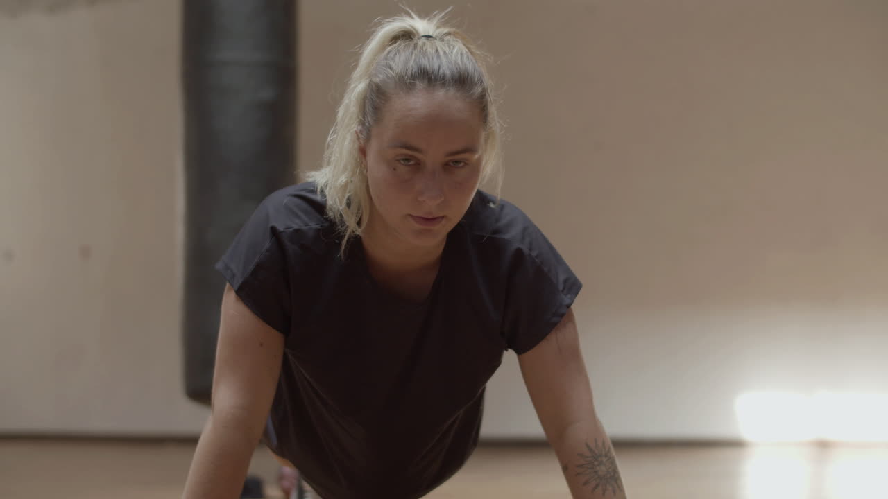 mujer segura de sí misma mirando a la cámara mientras hace flexiones en el gimnasio