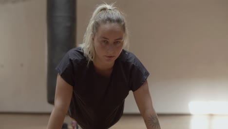 confident woman looking at camera while doing press-ups in gym